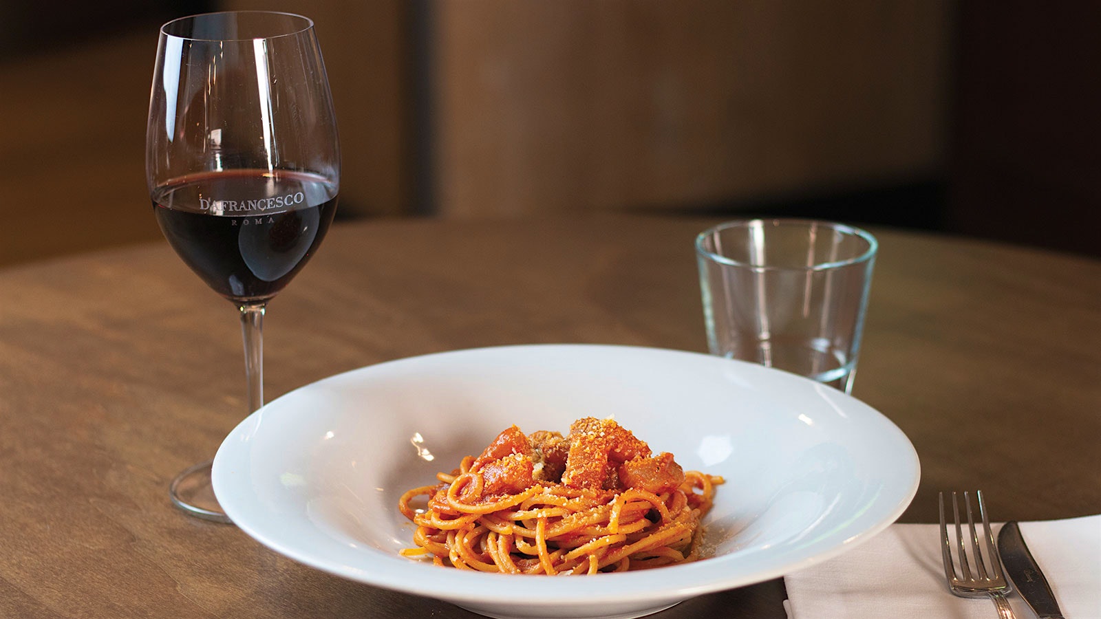 A plate of Spaghettoni all’amatriciana with a glass of red wine